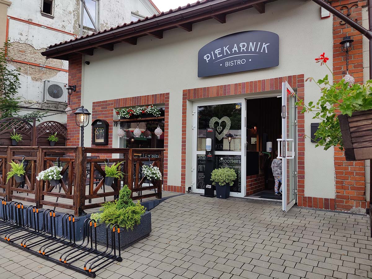 Fasada Bistro Piekarnik z szyldem, letnim ogródkiem i kwiatami